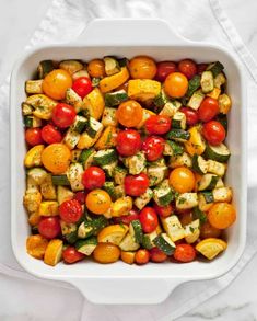 a white casserole dish filled with tomatoes, zucchini and other vegetables