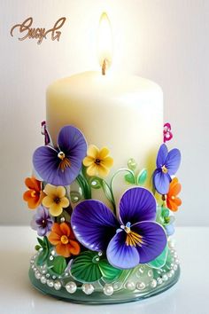 a white candle with purple and orange flowers on it, sitting on a glass stand