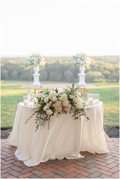 a table with white flowers and greenery on it is set up for an outdoor ceremony