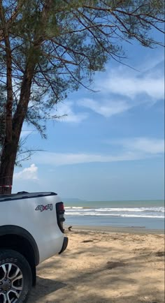 the truck is parked on the beach by the water's edge and there are trees in front of it