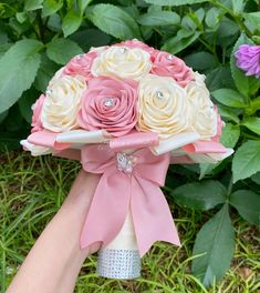 a bridal bouquet with pink, white and yellow roses is held by someone's hand