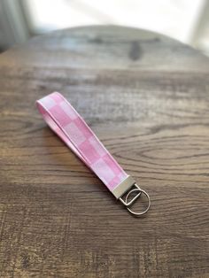 a pink and white checkered keychain sitting on top of a wooden table