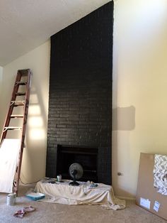 an empty room with a fireplace and a ladder next to it, in the process of being painted