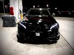 a black car is parked in front of a gas station with its hood up and lights on