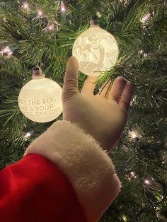 a person wearing a santa claus hat and gloves holding an ornament in front of a christmas tree