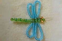 a blue and green beaded dragon brooch sitting on top of a white surface