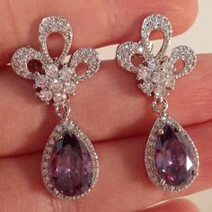 a pair of purple and white diamond earrings on someone's hand with diamonds around them