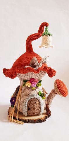 a crocheted mushroom house with a bell on it's roof and flowers around the top