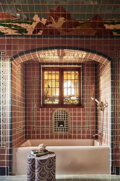 a bath tub sitting under a window next to a tiled wall and floor in a bathroom