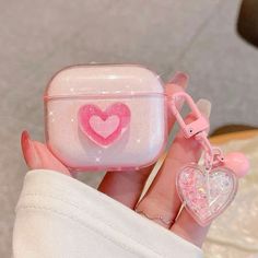 a hand holding a pink and white case with a heart charm attached to the front