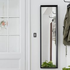 a mirror hanging on the side of a white wall next to a coat rack and potted plant