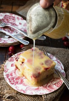 someone pours syrup over a piece of cake on a plate with cranberries