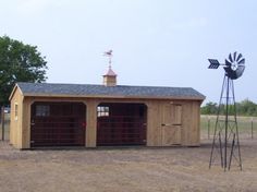 a horse barn with a windmill on the roof and two horses standing in front of it