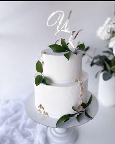 a three tiered cake with greenery on the top and initials on the side