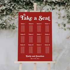 a red table plan sitting on top of a easel next to a wall covered in greenery