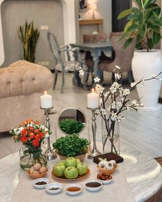 an arrangement of fruits and vegetables on a coffee table in a living room with candles