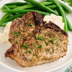 two pieces of meat on a plate with mashed potatoes and green beans