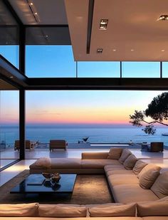 a living room with couches and large windows overlooking the ocean at sunset or dawn