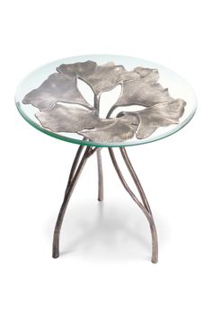 a glass table with metal legs and a flower design on the top, against a white background