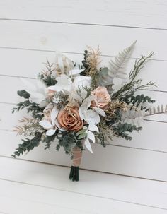 a bridal bouquet with flowers and greenery on a white wooden background in front of a wall