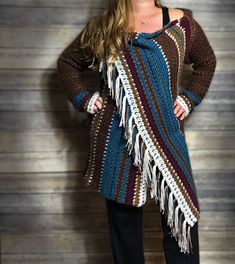 a woman standing in front of a wooden wall wearing a crocheted shawl