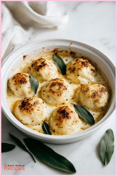 a white bowl filled with dumplings covered in cheese and sage leaf garnish