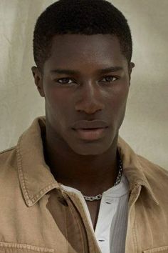 a young man in a tan jacket looking at the camera with a serious look on his face