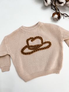 a sweater with a heart on the front and a chain across the chest, sitting next to cotton flowers