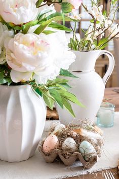 a vase with flowers and eggs on a table in front of a white pitcher filled with flowers