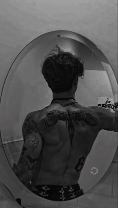 a man with tattoos standing in front of a mirror looking at his back and shoulder