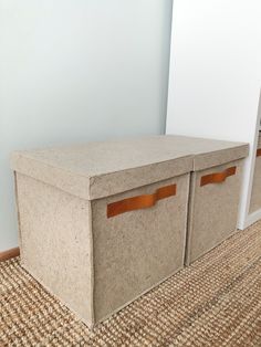 two storage bins sitting on the floor in front of a white wall with brown leather handles