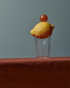 a lemon and cherry sitting on top of a cupcake in a glass vase with a red table cloth