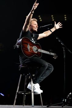 a man sitting on top of a stool with his hand in the air while holding a guitar