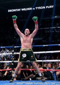 a man standing on top of a boxing ring holding up his hands in the air