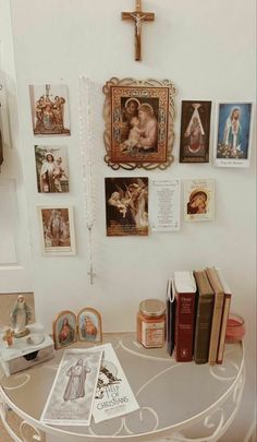 a white table topped with lots of books next to a cross and pictures on the wall