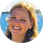 a smiling woman with large hoop earrings in front of the ocean and mountains behind her