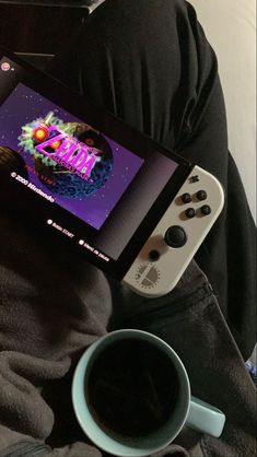 a nintendo wii game system sitting on top of someone's lap next to a cup of coffee