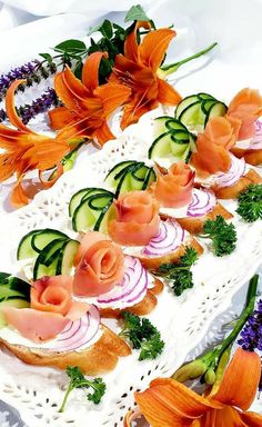 an arrangement of food is displayed on a white platter with orange lilies and purple flowers