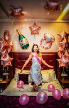 a woman standing on top of a bed with balloons and champagne bottles in the air