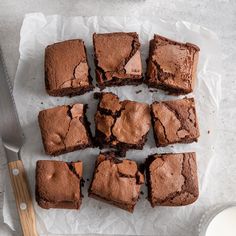 chocolate brownies cut into squares on top of wax paper next to a knife and glass of milk