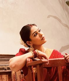 a woman in a red sari leaning on a wooden chair with her arms crossed