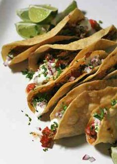 some tacos are on a white plate with lime wedges and sour cream sauce