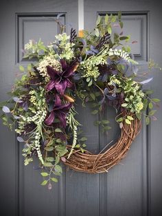 a wreath with purple flowers and greenery hangs on the front door's gray door