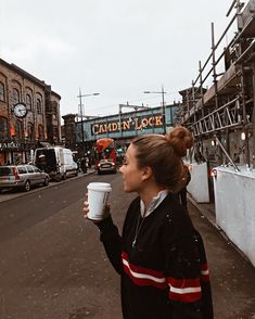 a woman standing on the side of a road holding a coffee cup in her hand