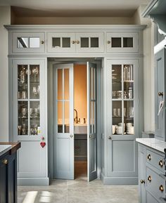 an open door leading into a kitchen with white cabinets and glass doors on both sides