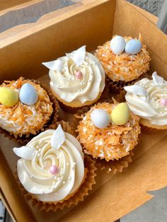 four cupcakes in a box with white frosting and decorated eggs on top