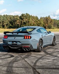 the rear end of a silver sports car on a parking lot with trees in the background