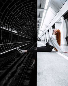 a woman with red hair sitting on the ground next to train tracks and looking up