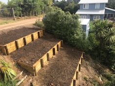 several wooden raised garden beds in front of a house with trees and bushes around them