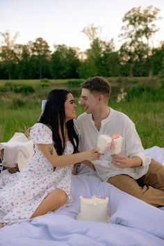 a young man and woman sitting on a blanket holding cake in front of each other